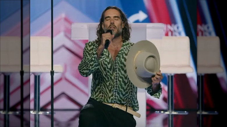 Russell Brand kneeling and speaking into a microphone