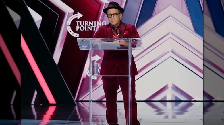 Rob Schneider speaking at a podium