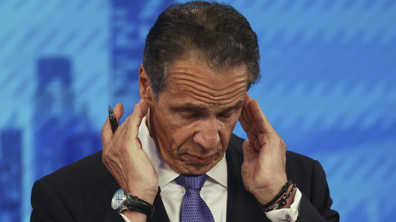 Andrew Cuomo touching his ears during an interview with a pen in his hand