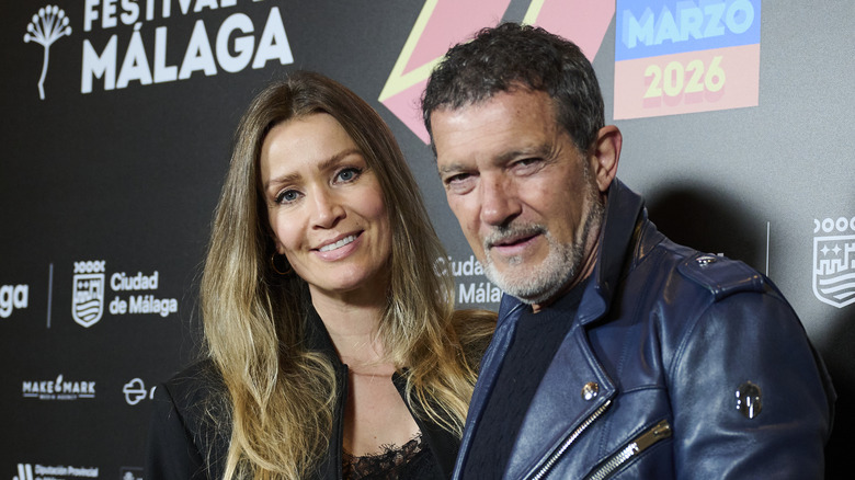 Nicole Kimpel posing with Antonio Banderas wearing a leather jacket against a black background.