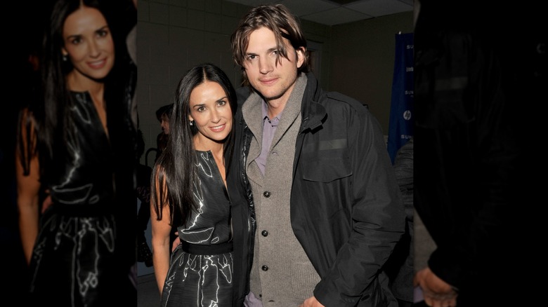 Ashton Kutcher and Demi Moore posing together in a black coat and shiny black dress, respectively.