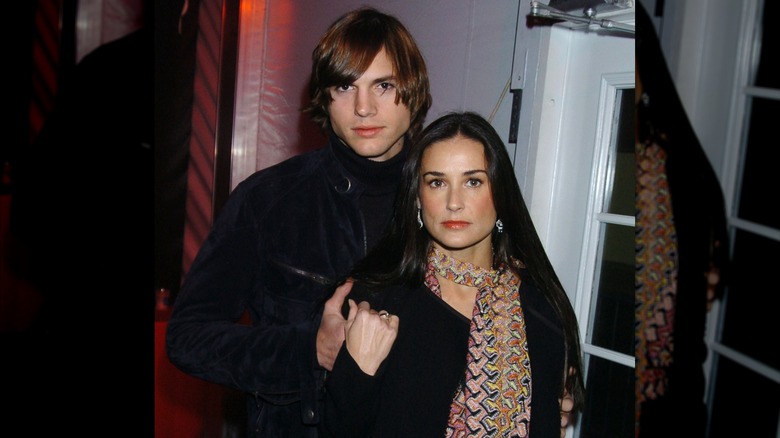 Ashton Kutcher standing behind Demi Moore while holding hands.