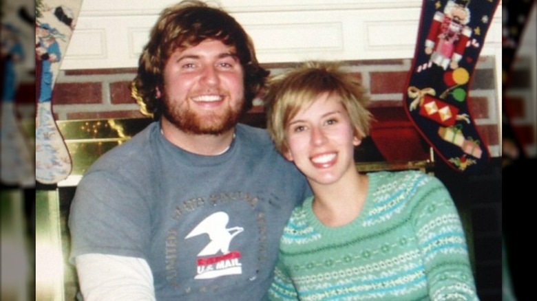 Erin and Ben Napier seated in front of a fireplace with Christmas stockings hung over it.