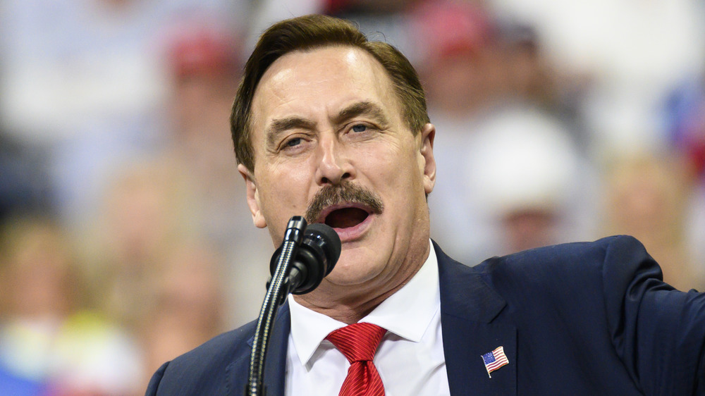 Mike Lindell, speaking at a podium, mouth open, in a suit