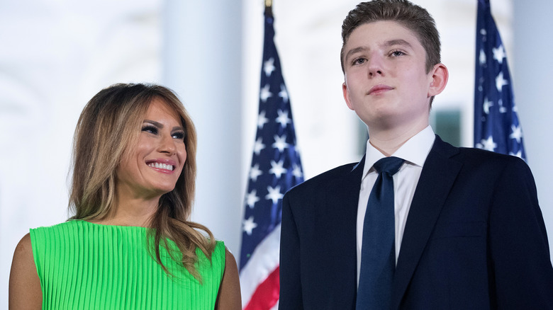 Melania Trump and Barron Trump standing in front of flags