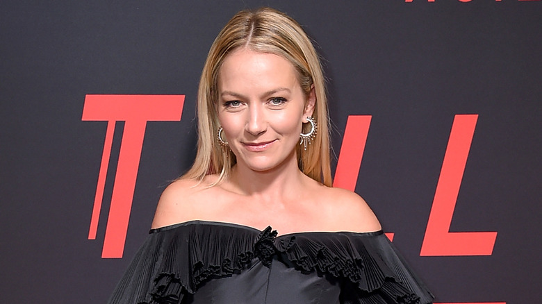 Becki Newton, wearing a black outfit with gathered detailing, smiles at the camera.