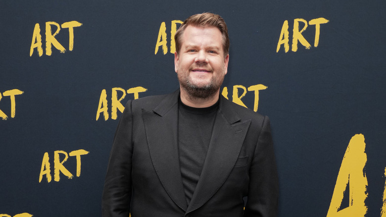 James Corden in a black blazer standing in front of a step and repeat for Art