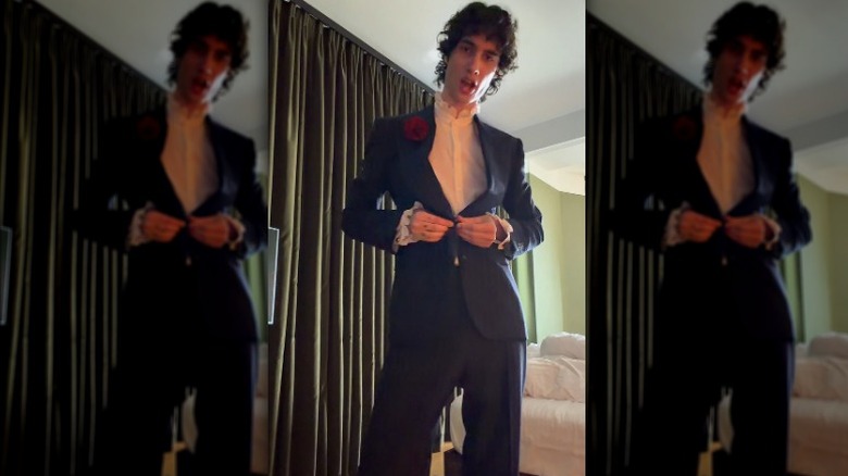 Sombr buttoning up his suit jacket.