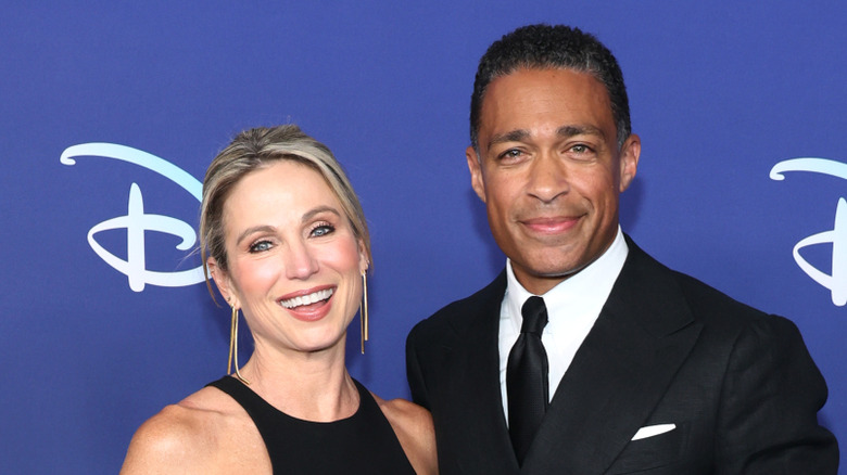 Amy Robach in a black dress and TJ Holmes in a black suit and tie, smiling.