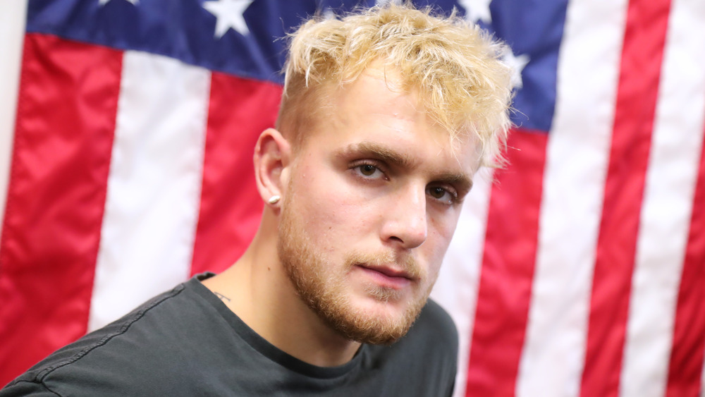 Jake Paul looking serious in front of an American Flag 