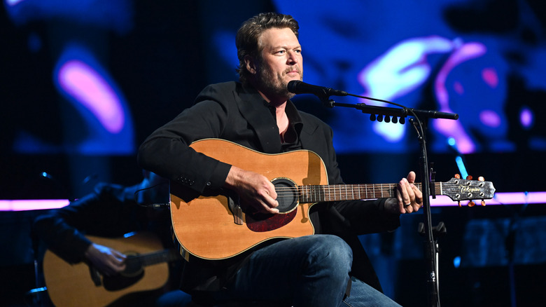 Blake Shelton seated and playing guitar