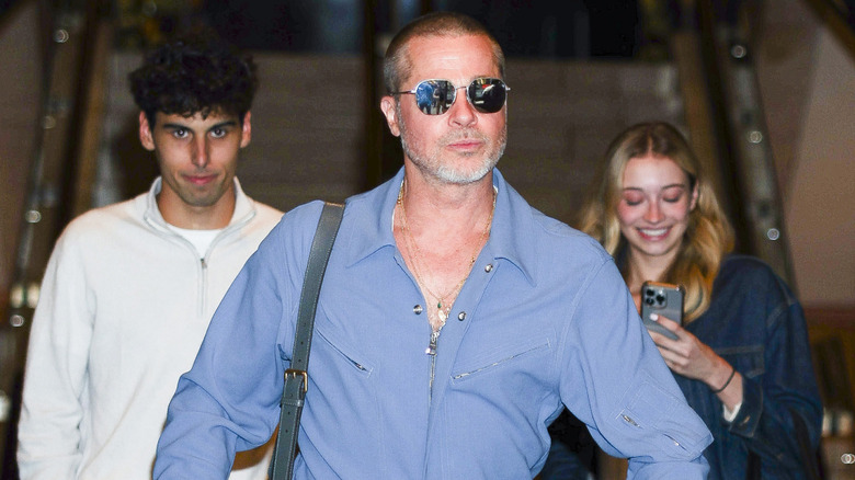 Brad Pitt exiting a building with sunglasses on and a light blue shirt
