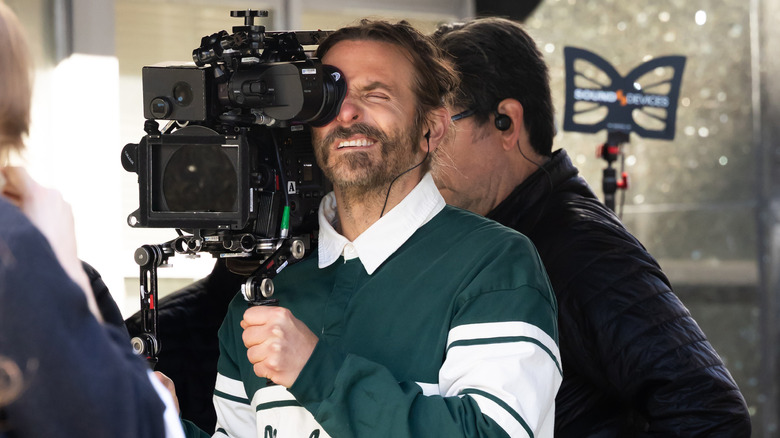 Bradley Cooper looking through a viewfinder and holding a camera