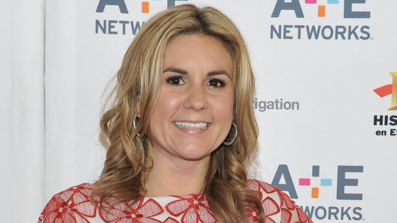 Sporting a patterned dress and hoop earrings, Brandi Passante flashes a wide smile.