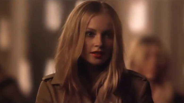 Wearing a beige trench coat and striking red lipstick, Hannah Dodd looks away from the camera.