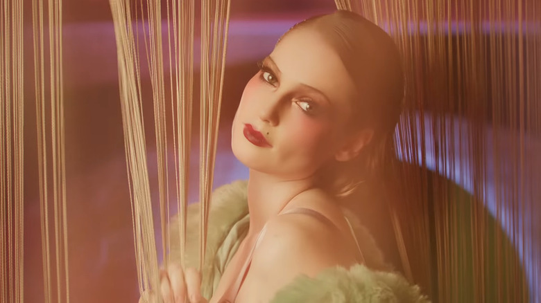 Wearing bold makeup, Hannah Dodd looks into the lens while her head is tilted to the side.