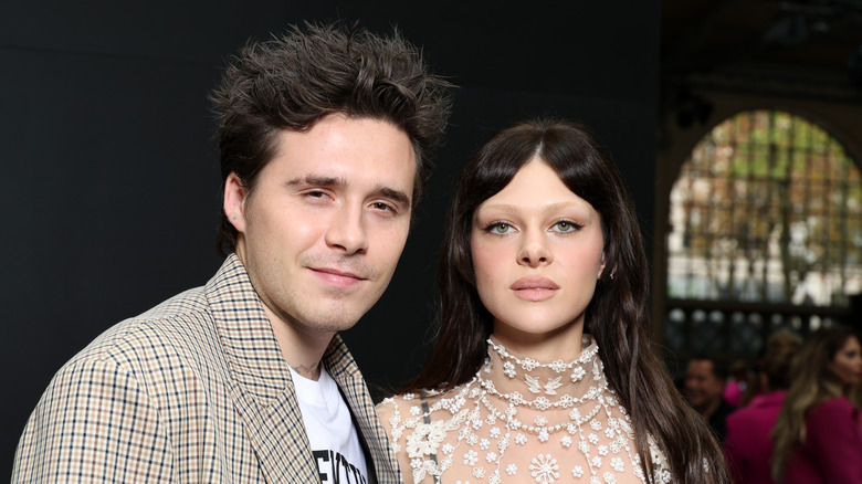 Brooklyn Beckham smiles gently as Nicola Peltz gives the camera an icy stare.