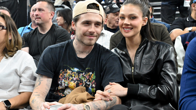 A cheerful Nicola Peltz wraps her arms around Brooklyn Beckham at a game.