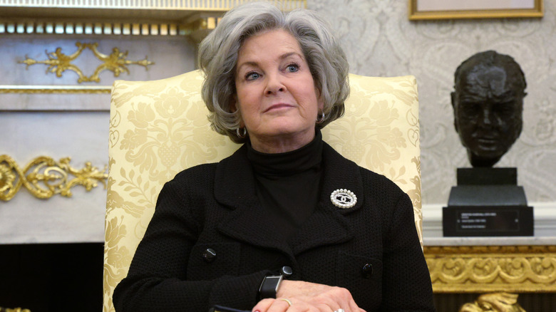 Susie Wiles sitting in the Oval Office with her hands crossed in an all-black outfit