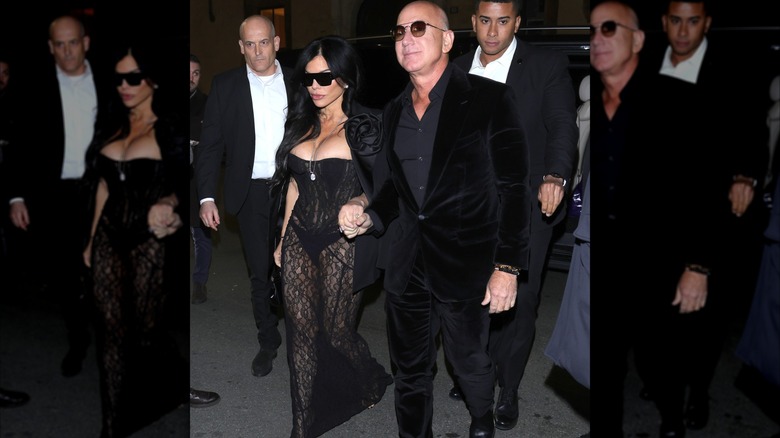 Jeff Besos holding Lauren Sánchez's hand who is wearing a very tight black corset dress