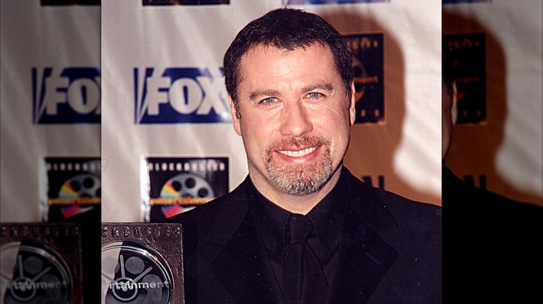 John Travolta posing with an award in the 1990s.