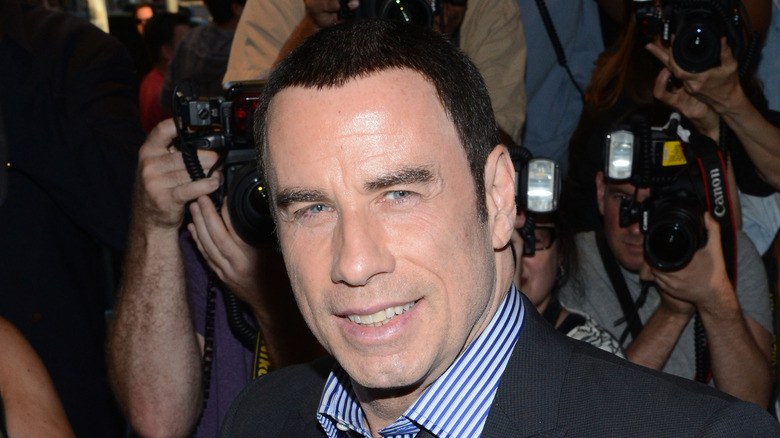 John Travolta flanked by photographers on the red carpet.