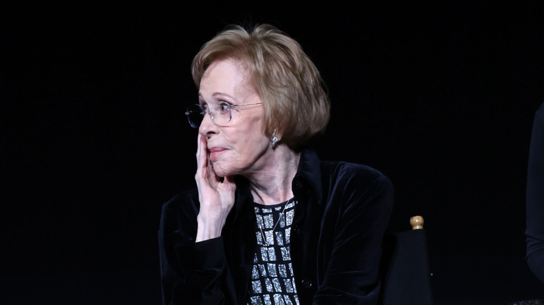 Carol Burnett sitting with her head resting on her hand, looking pensive against a black background.