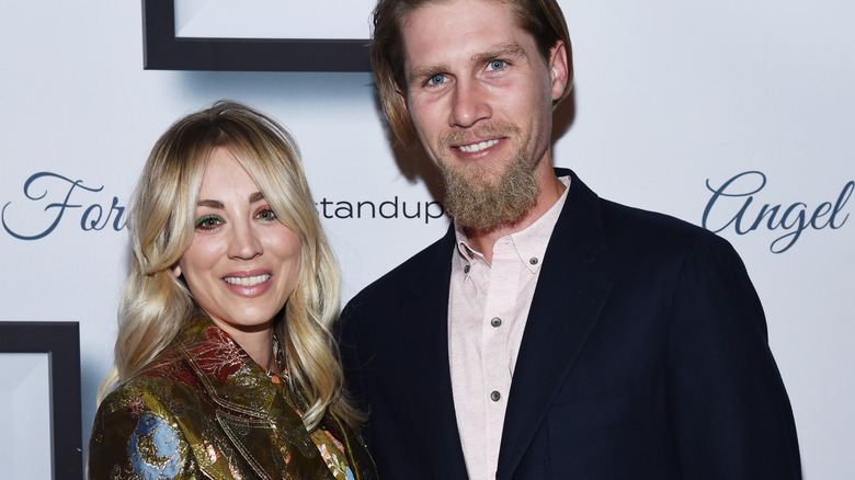 Kaley Cuoco and Karl Cook in front of a promotional wall, smiling