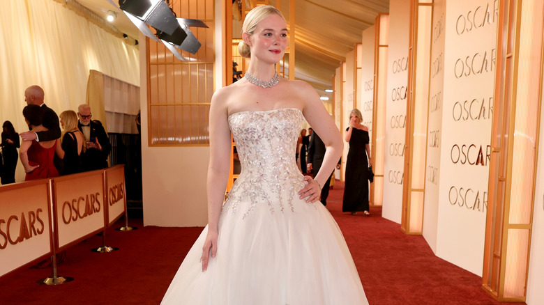 Elle Fanning posing on the red carpet ahead of the 98th Academy Awards in a white bejeweled strapless gown