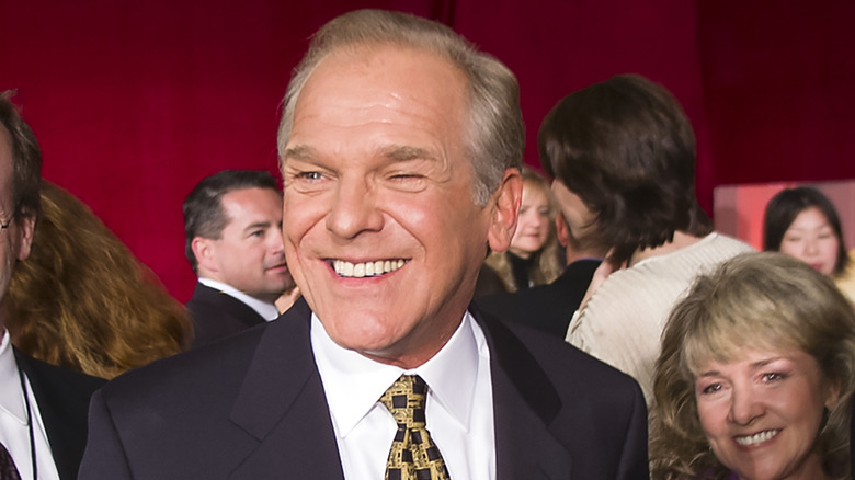 John Spencer wearing a black suit and yellow and black patterned tie