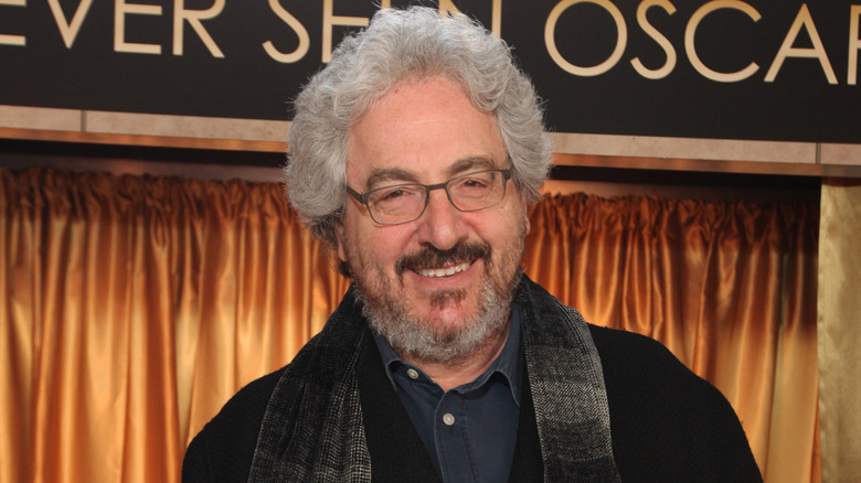 Harold Ramis wearing glasses, a black jacket, blue collared shirt and a black and silver scarf