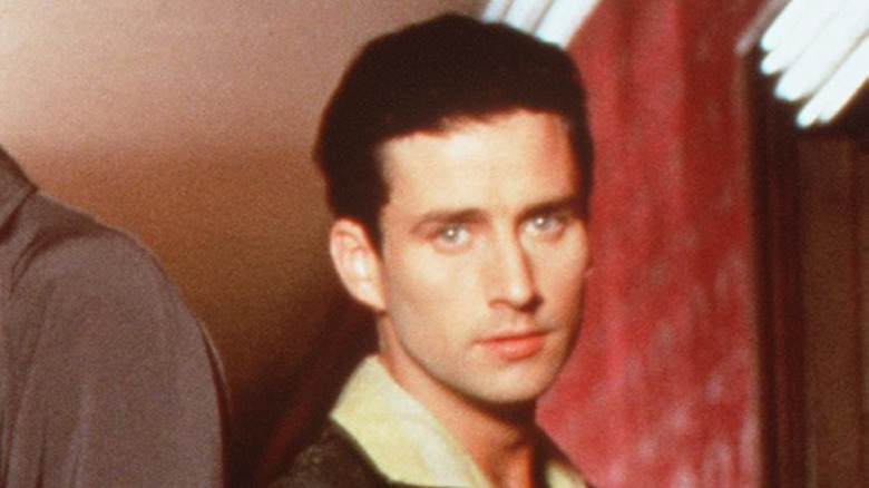 Glenn Quinn wearing.a brown jacket and cream collared shirt