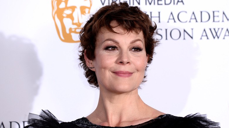 Helen McCrory with short brown hair wearing a black dress with short frilled sleeves