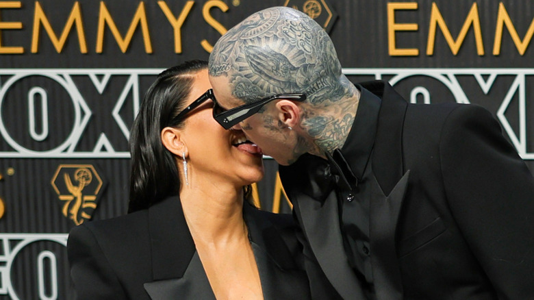 Kourtney Kardashian and Travis Barker wearing matching black suits and locking tongues
