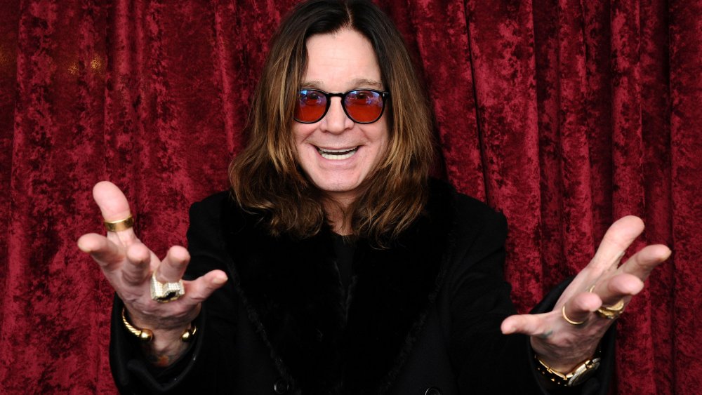 Ozzy Osbourne in front of velvet wall, hands reaching out