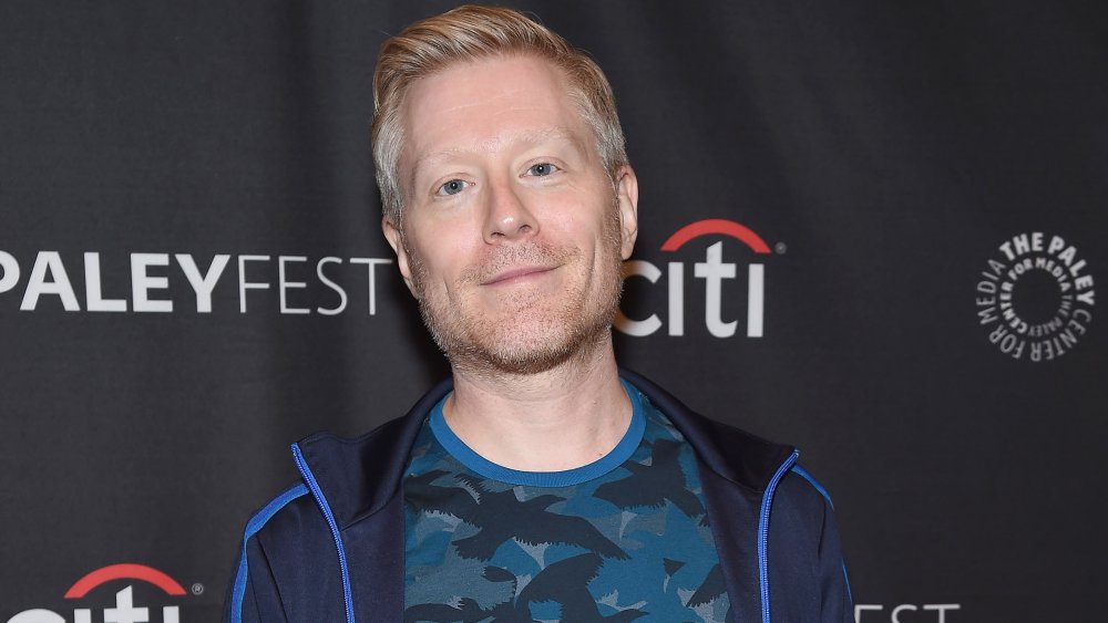 Anthony Rapp grinning at the camera in a blue outfit
