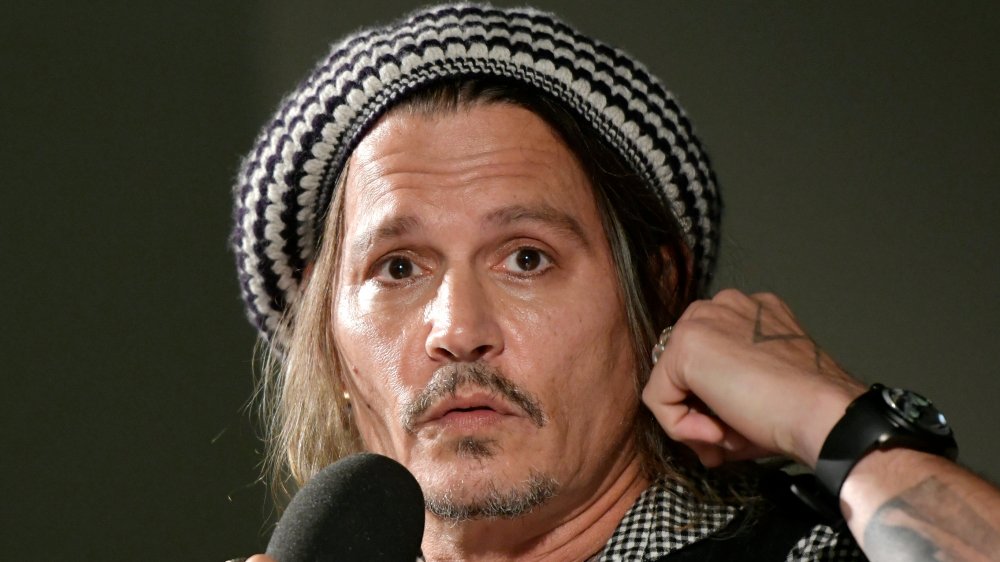 Johnny Depp wearing a black-and-white knitted hat, looking shocked while speaking into a mic