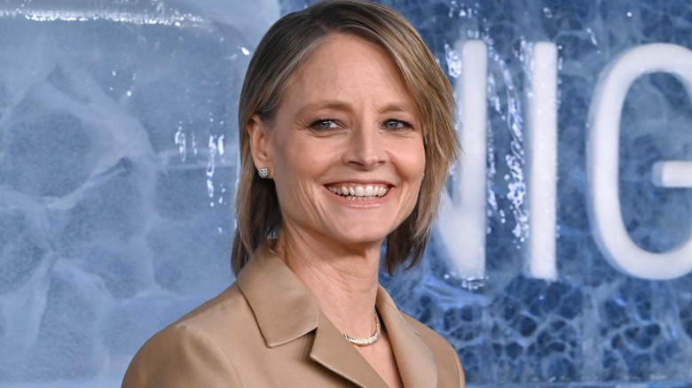 Jodie Foster smiling in brown coat