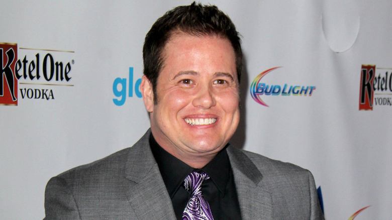 Chaz Bono wearing a grey suit jacket, black collared shirt and purple patterned tie at a red carpet event