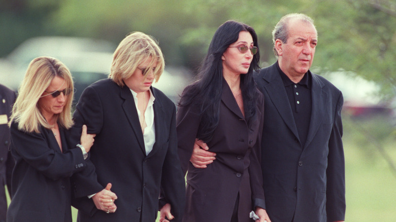 Chaz Bono and Cher wearing black suits accompanied by two other people in black while attending Sonny Bono's funeral