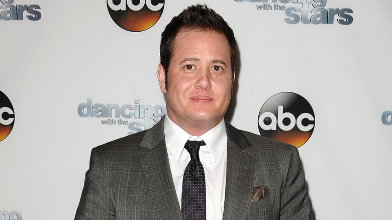 Chaz Bono wearing a grey striped suit jacket, white collared shirt and black and white dotted tie at a red carpet event