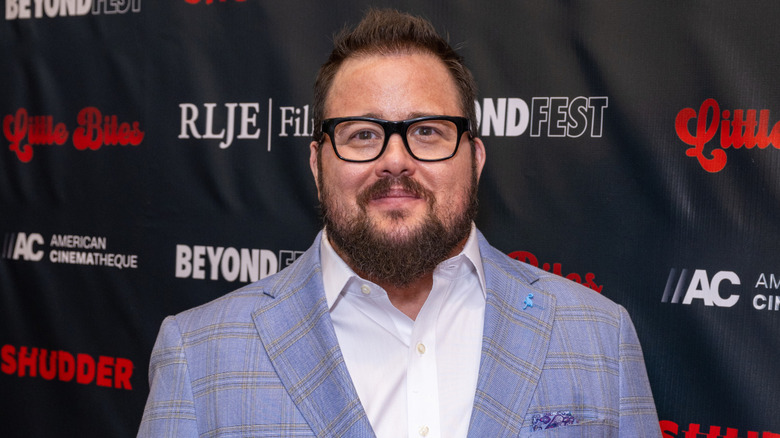 Chaz Bono wearing a blue and grey pinstriped suit, white collared shirt, and black rimmed glasses
