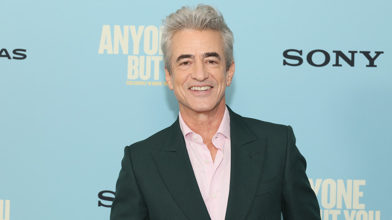 Dermot Mulroney smiling while posing at the Anyone But You premiere in a black suit