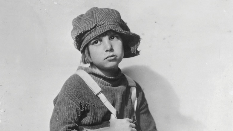 Sporting a hat, a sweater and suspenders, young Jackie Coogan looks away from the camera