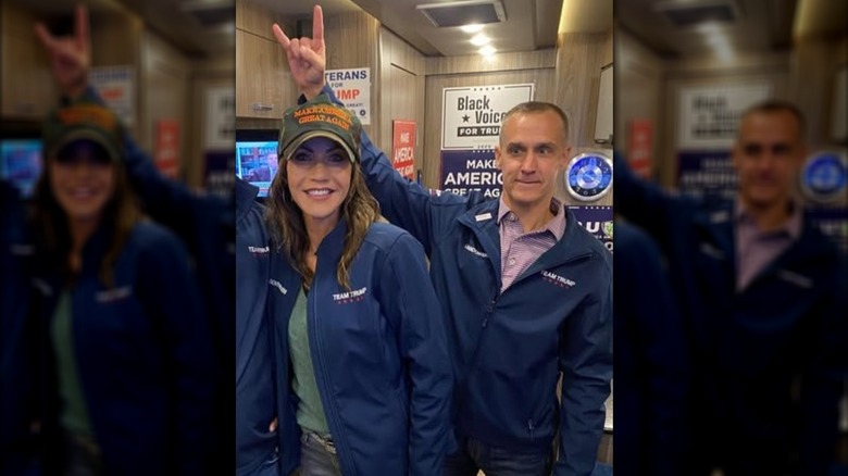 Corey Lewandowski making the sign of the horns over Kristi Noem's head.