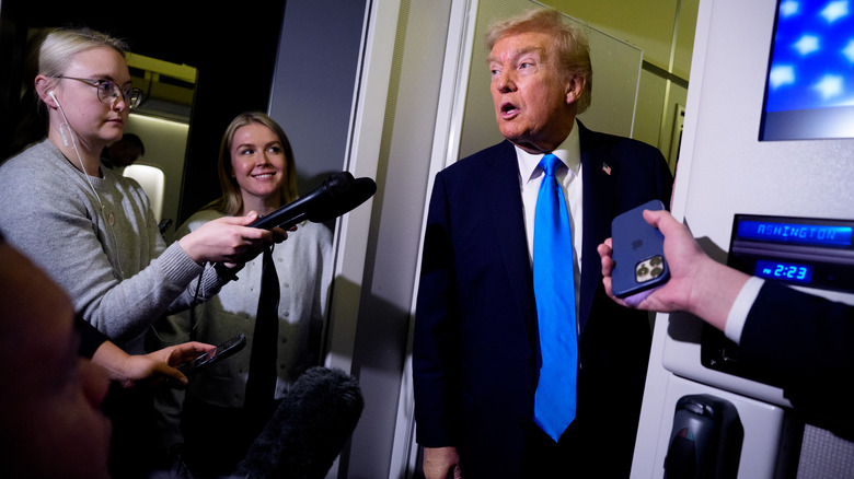 Donald Trump addresses the press on Air Force One as Karoline Leavitt looks on.