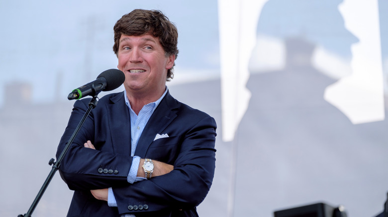 Tucker Carlson with arms crossed behind microphone