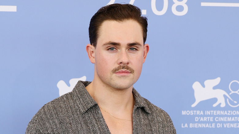 Dacre Montgomery wearing an open v-neck gray collared shirt