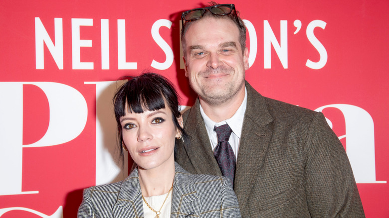 Lily Allen wearing a black and white striped jacket beside David Harbour wearing a brown jacket and glasses