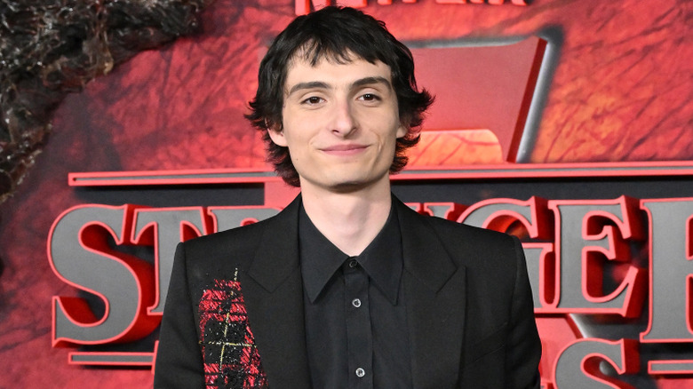 Finn Wolfhard wearing a black blazer with a black button down collared shirt